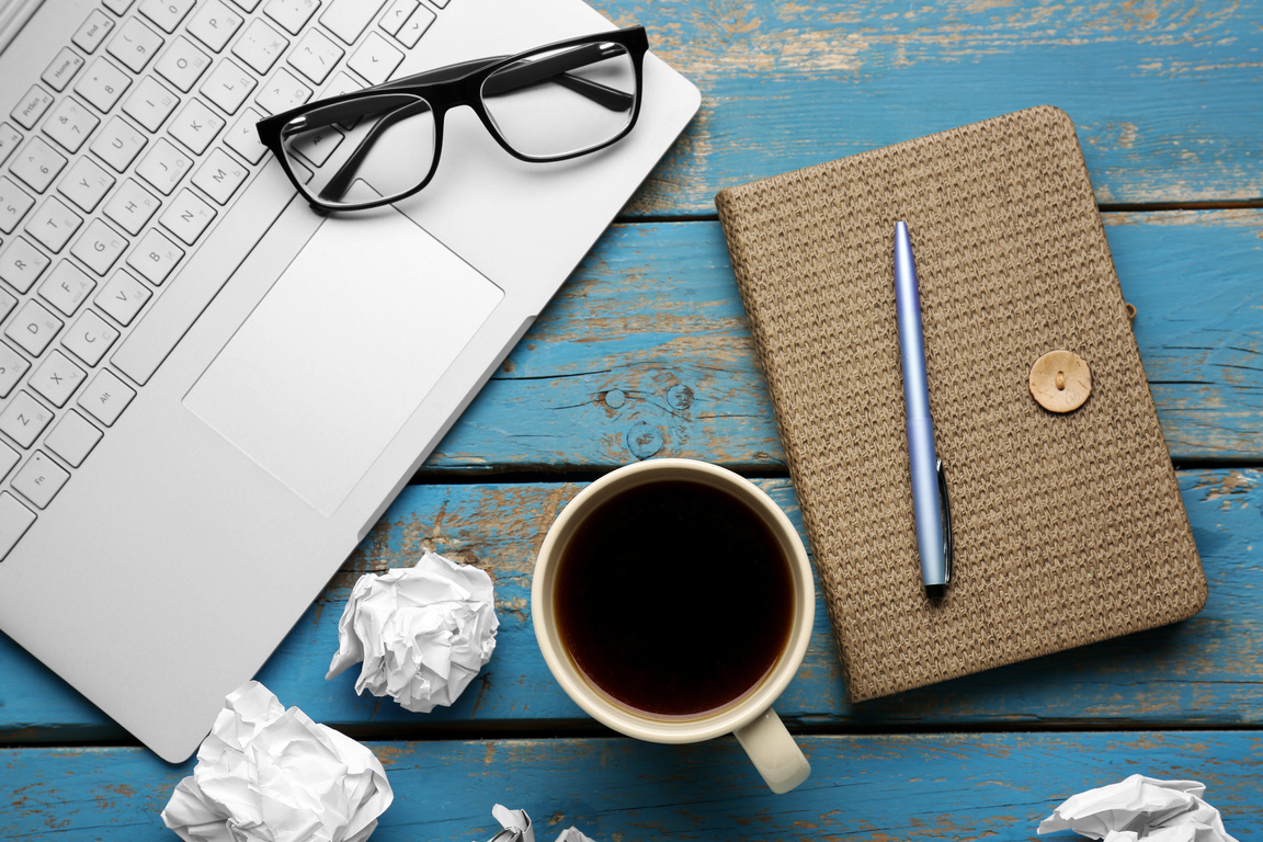Notebook, Pen, Cup of Coffee, Eyeglasses, Laptop and Crumpled Paper on Color Wooden Background, Closeup