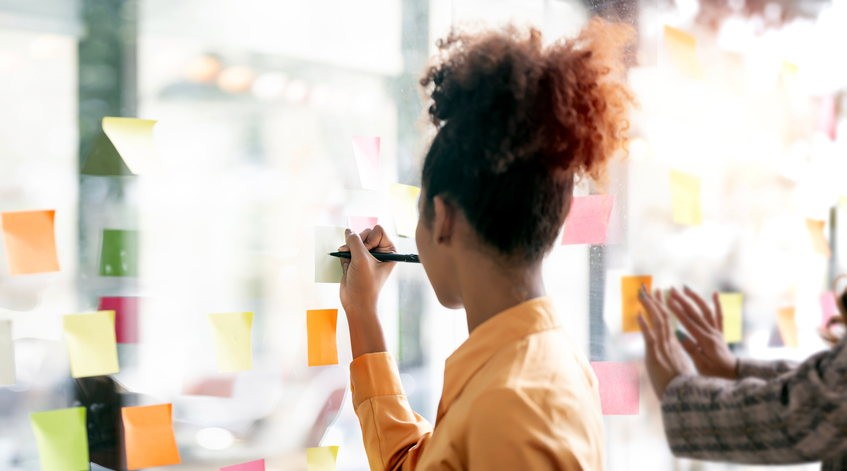 Young businesswoman creative team using post it notes in glass w